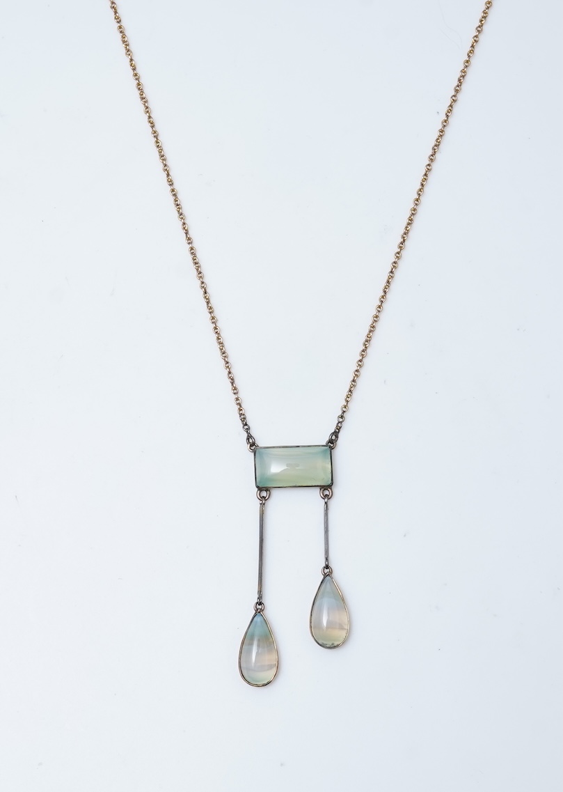 An Edwardian agate necklace, early 20th century, of negligée design, centring on a rectangular cabochon of translucent pale green agate, suspending a pair of pendants of unequal lengths, culminating in pear-shaped caboch